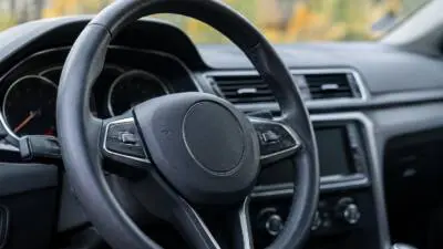 KI-generiertes Bild: Ein schwarzes Lenkrad vor dem Armaturenbrett eines Autos.