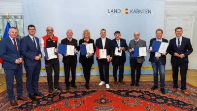 Geehrte präsentieren bei einer Feier in Kärnten ihre Urkunden und Auszeichnungen.