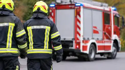 KI-generiertes Bild: Personen in dunkler Schutzkleidung und gelben Helmen vor einem roten Einsatzfahrzeug.