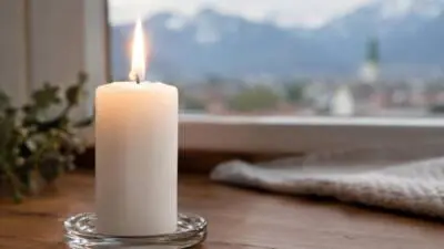 KI-generiertes Bild: Eine brennende weiße Kerze steht auf einem Glasteller vor einem Fenster mit Bergblick.
