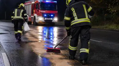 KI-generiertes Bild: Eine Person mit Besen auf nasser Straße, dahinter ein rotes Einsatzfahrzeug.
