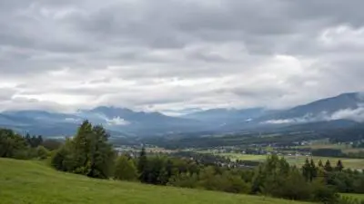 KI-Symbolbild: Dichte Wolken über bewaldeten Bergen und einem grünen Tal.