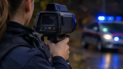 KI-Symbolbild: Eine uniformierte Person hält ein Messgerät vor einem Auto mit blauem Blaulicht.