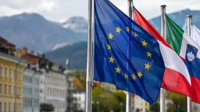 KI-generiertes Bild: Europäische Flaggen wehen vor einer alpinen Stadtkulisse.