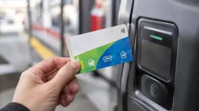KI-Symbolbild: Eine Hand hält eine blau-grüne Fahrkarte an ein kontaktloses Lesegerät.