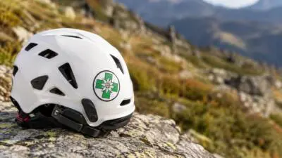 KI-Symbolbild: Ein weißer Helm liegt auf einem Felsen vor alpiner Bergkulisse.