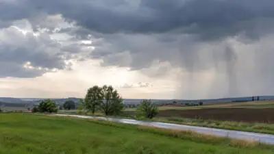 KI-Symbolbild: Dunkle Wolken und Regen über Feldern und einer Landstraße.