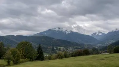 Bewölkter Himmel über bewaldeten Bergen und einem grünen Tal mit verstreuten Häusern