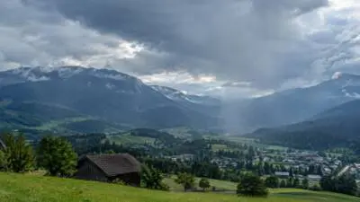 KI-Symbolbild: Regenwolken ziehen über ein grünes Bergtal.