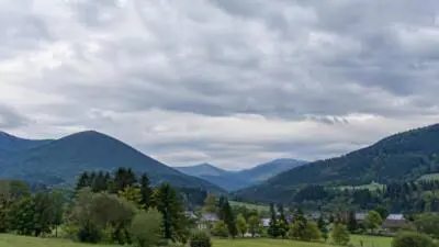 Dichte graue Wolken über bewaldeten Bergen und einem grünen Tal