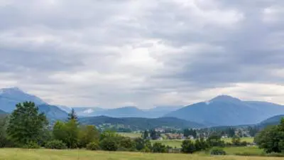 Bewölkter Himmel über Bergen, einem grünen Tal und einer offenen Wiese