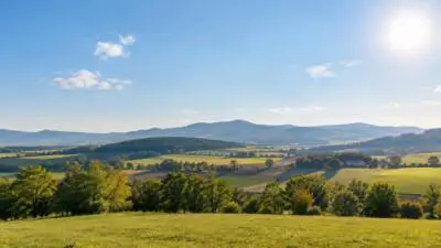 Sonnige Landschaft mit grünen Feldern, bewaldeten Hügeln und blauem Himmel