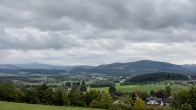 Dunkle Wolken über grünen Feldern, bewaldeten Hügeln und einem Dorf