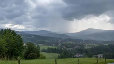 KI-Symbolbild: Dunkle Wolken und Regen über einer grünen Hügellandschaft.