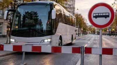 KI-Symbolbild: Ein weißer Reisebus steht hinter einer Schranke neben einem Busfahrverbotsschild.
