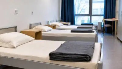 KI-generiertes Bild: Ein Schlafraum mit weiß bezogenen Betten und gefalteten grauen Decken.