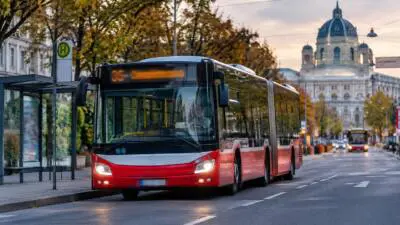 KI-generiertes Bild: Ein rot-weißer Gelenkbus steht an einer Haltestelle.