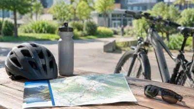 KI-Symbolbild: Fahrradhelm, Trinkflasche und Karte auf einem Holztisch neben einem Fahrrad.