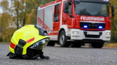 KI-generiertes Bild: Ein gelber Feuerwehrhelm liegt vor einem roten Feuerwehrfahrzeug.