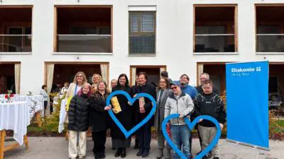 Menschen halten blaue Herzformen vor einem Wohngebäude mit Diakonie-Banner.