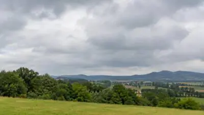 KI-Symbolbild: Dichte Wolken über einer grünen, hügeligen Landschaft.