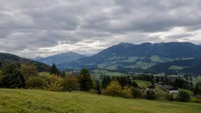 KI-Symbolbild: Grüne Wiesen und bewaldete Berge unter dichtem Wolkenhimmel.