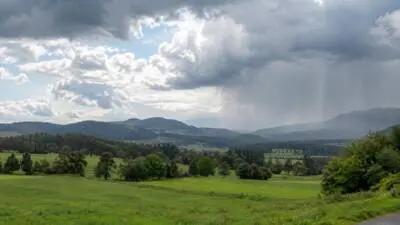 KI-generiertes Bild: Dunkle Regenwolken ziehen über eine grüne Hügellandschaft.