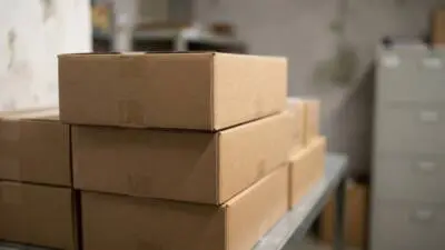 KI-generiertes Bild: Braune Kartons stehen gestapelt auf einem Metalltisch.