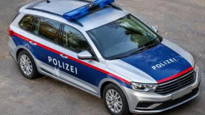 KI-generiertes Bild: Ein silberner Polizeikombi mit blauem Lichtbalken steht auf einer Straße.