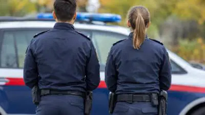 KI-Symbolbild: Zwei uniformierte Personen stehen vor einem Fahrzeug mit Blaulicht.