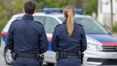 Uniformierte Personen von hinten vor einem weiß-blauen Auto mit Blaulicht
