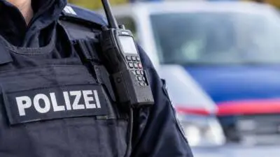 KI-generiertes Bild: Eine Polizeikraft mit Funkgerät vor einem unscharfen Polizeifahrzeug.