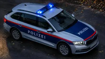 KI-generiertes Bild: Ein silber-blaues Polizeiauto mit eingeschaltetem Blaulicht steht auf dunklem Asphalt.
