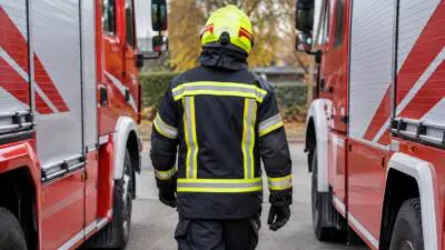 KI-generiertes Bild: Eine Feuerwehrkraft steht zwischen roten Feuerwehrfahrzeugen.