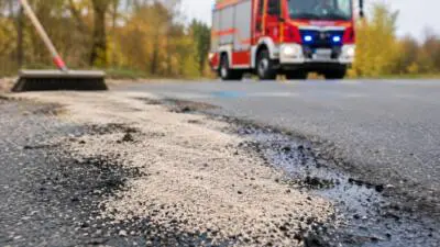 KI-generiertes Bild: Ein rotes Feuerwehrfahrzeug steht hinter hellen Streukörnern auf einer Straße.