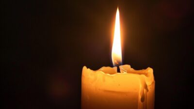Eine brennende gelbe Kerze mit geschmolzenem Wachs und heller Flamme auf dunklem Hintergrund.