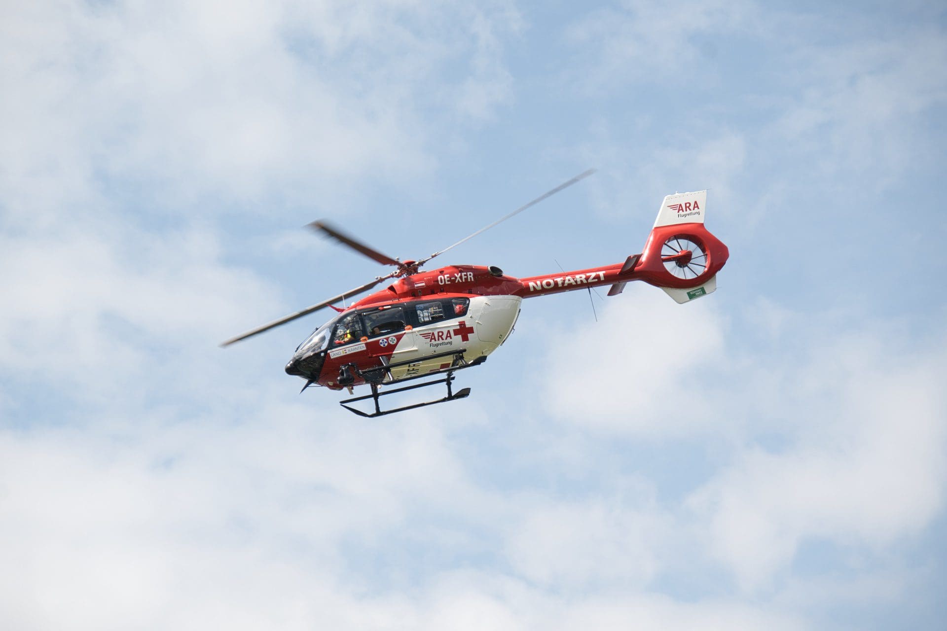 Roter und weißer Rettungshubschrauber der ARA Flugrettung mit Kennung OE-XFR fliegt vor blauem Himmel