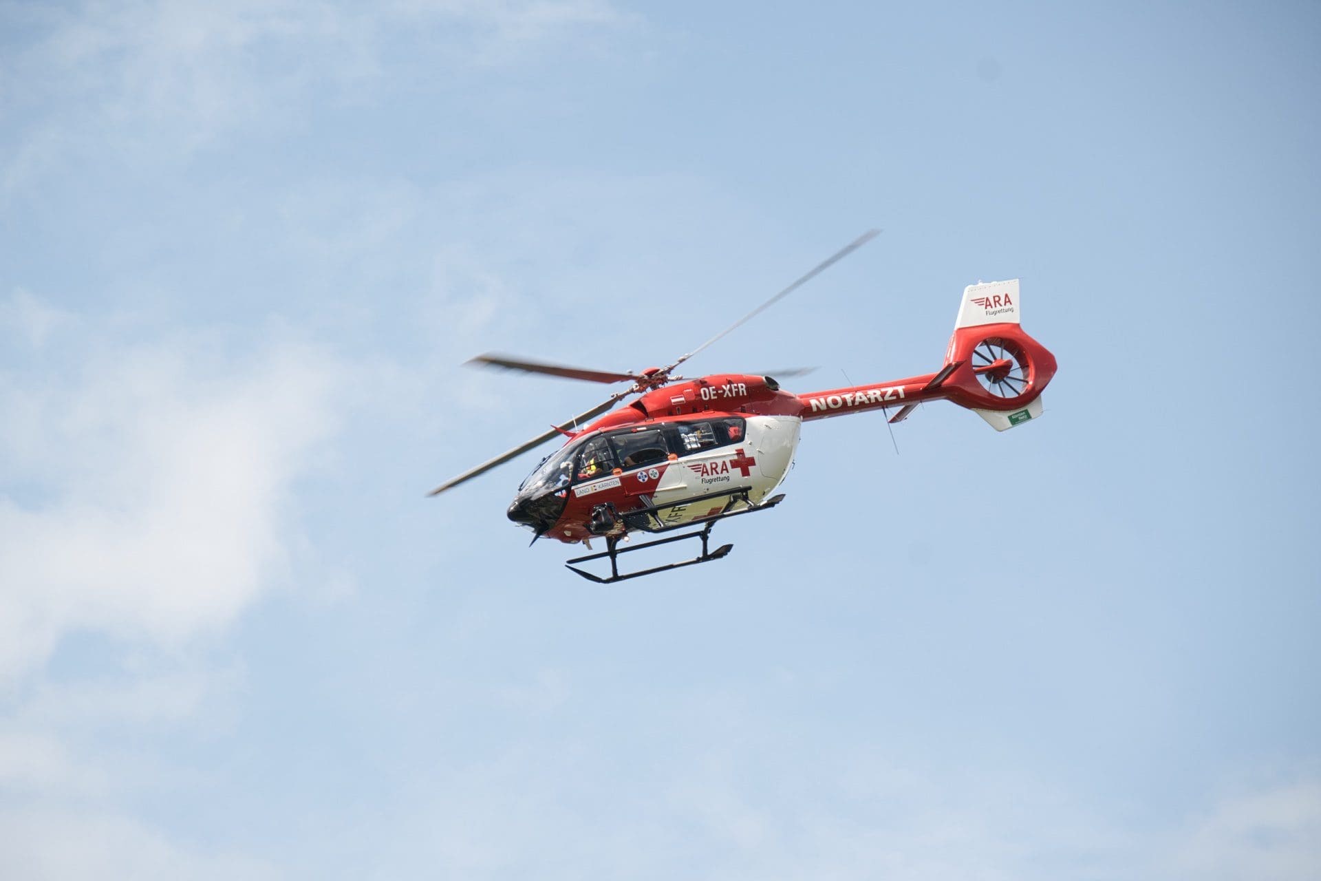 Roter und weißer Rettungshubschrauber der ARA Flugrettung fliegt vor blauem Himmel