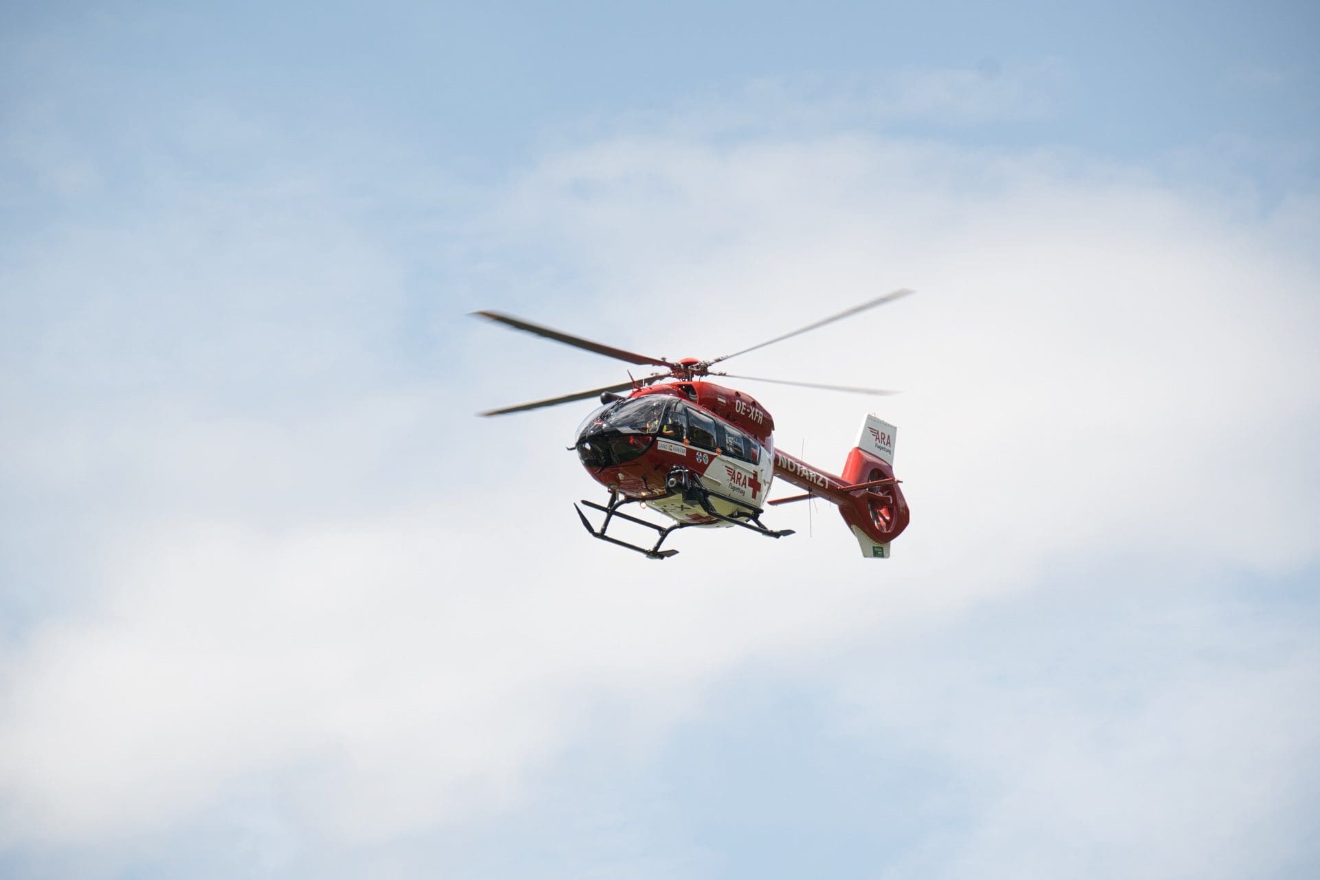 Roter und weißer Rettungshubschrauber der ARA Flugrettung fliegt vor blauem Himmel