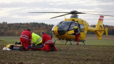 Rettungskräfte versorgen Verletzten auf Trage neben gelbem Hubschrauber auf Acker