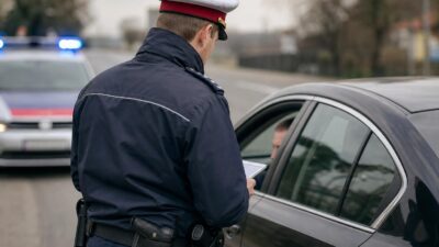 Polizist in Uniform steht neben einem schwarzen Auto und kontrolliert den Fahrer