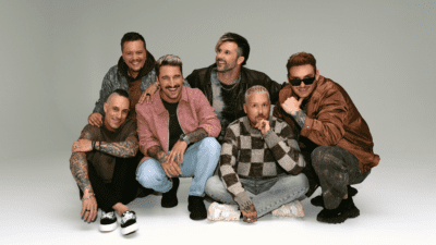 Fünf Männer der Band Electric Callboy posieren gemeinsam vor einem grauen Hintergrund