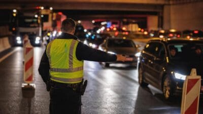 Polizist in gelber Warnweste dirigiert Fahrzeuge auf nächtlicher Autobahn bei Baustelle