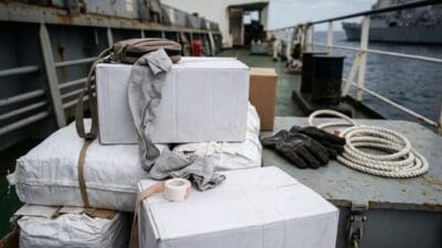 Stapel weißer Kartons und Säcke mit Handschuhen und Seilen auf dem Deck eines Schiffes auf dem Meer