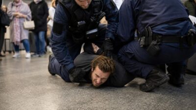 Zwei Polizisten fixieren einen Mann am Boden eines Flughafenterminals.