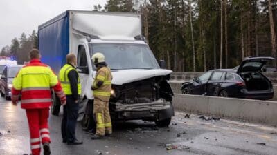 Rettungskräfte und Feuerwehrmann vor beschädigtem Lkw nach Unfall auf Autobahn