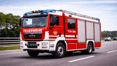 Rotes und weißes Feuerwehrauto mit blauen Blinklichtern auf einer Autobahn