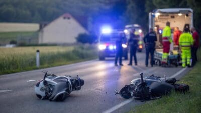 Zwei umgestürzte Mopeds liegen auf einer Landstraße nach einem Unfall mit Blaulicht im Hintergrund.