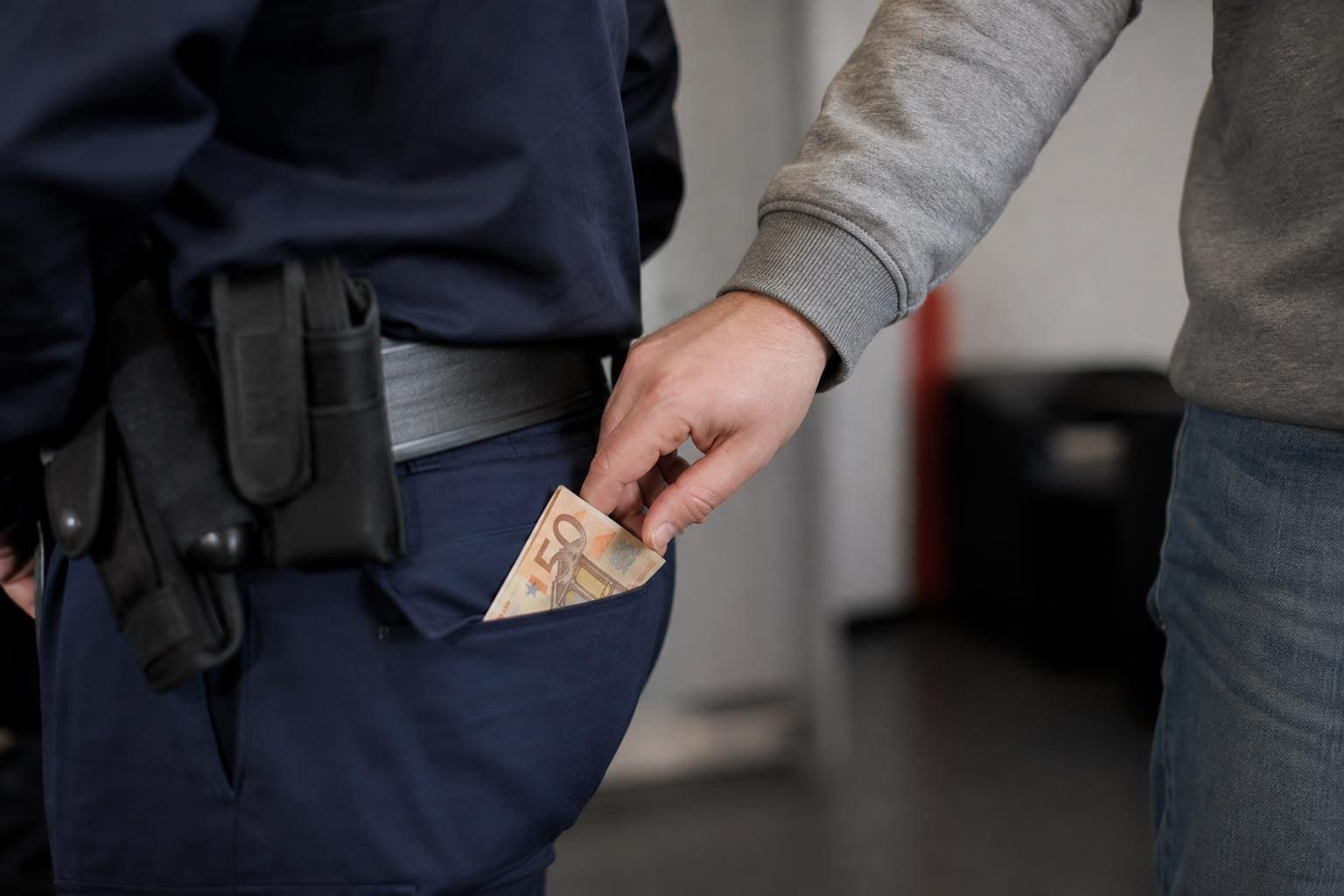 Eine Hand steckt einen 50-Euro-Schein in die Hosentasche eines Polizisten