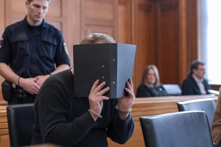 Angeklagter im Gerichtssaal verdeckt sein Gesicht mit einem schwarzen Aktenordner während einer Verhandlung in Klagenfurt